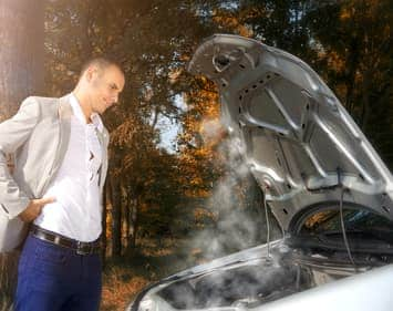 Businessman standing by the car with hood open trying to solve the problem. Smoke coming out of the engine.